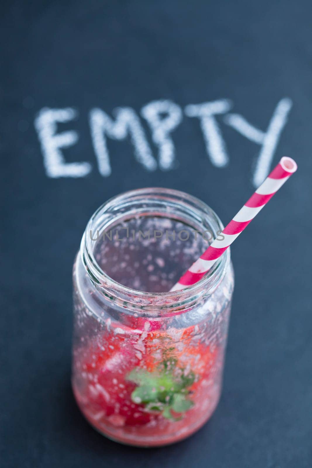Empty strawberry smoothie glass with striped straw and chalk text on dark background