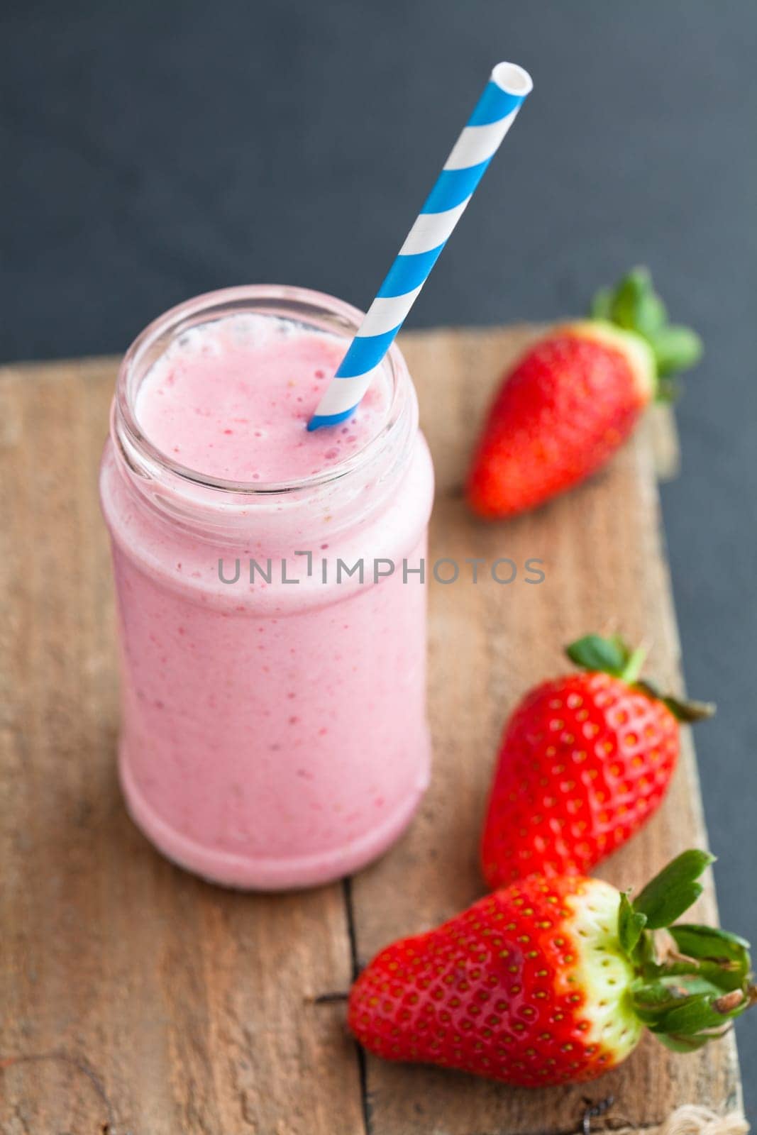 Strawberry smoothie with striped straw and whole strawberries on wooden serving tray