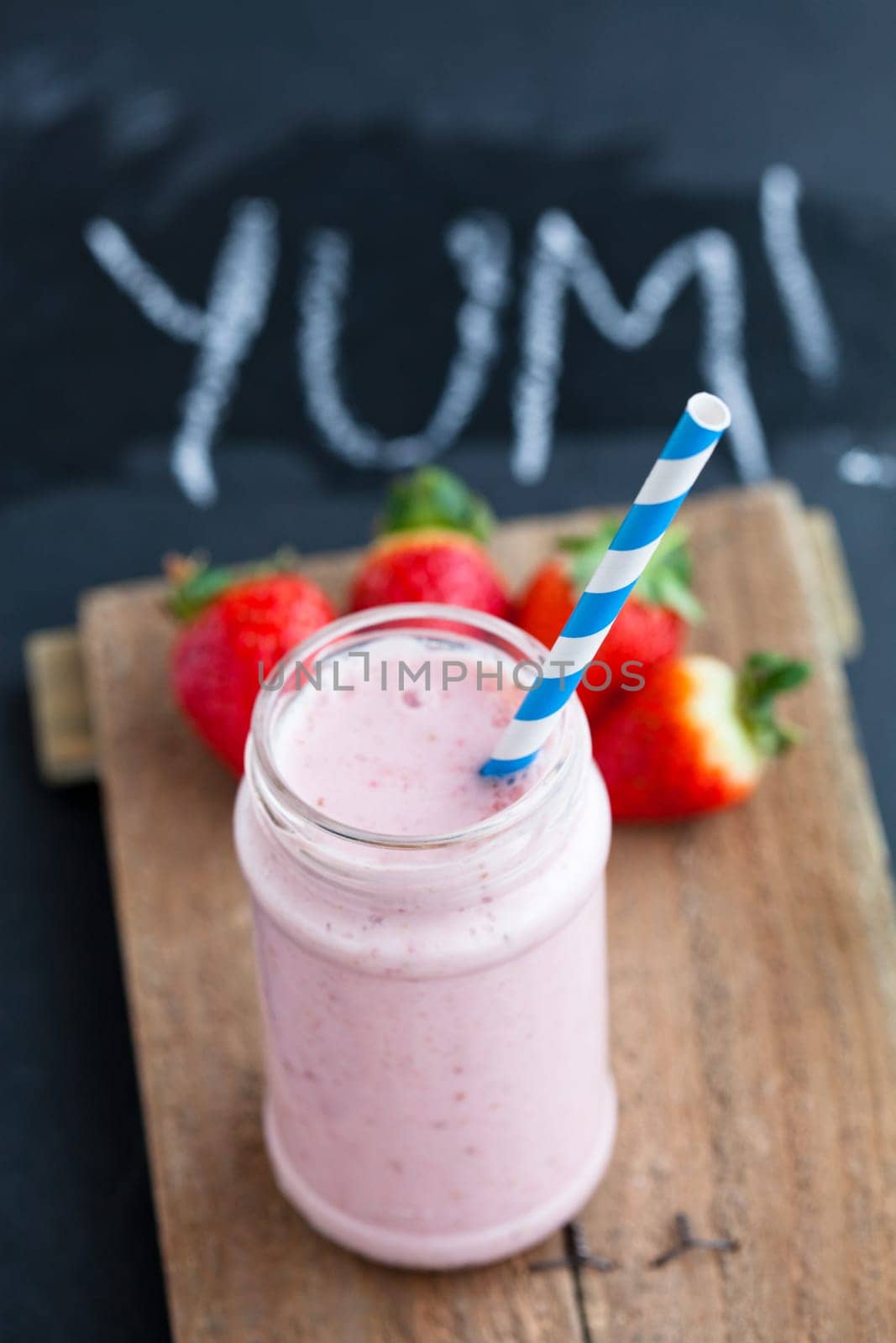 Strawberry smoothie with striped straw and whole strawberries on wooden serving tray