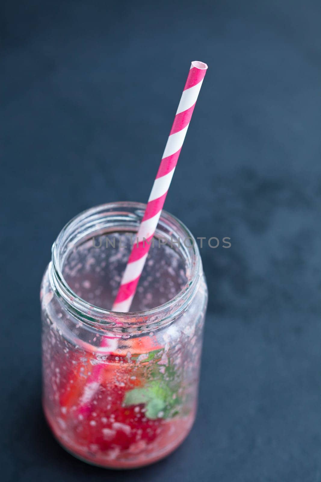 Empty strawberry smoothie glass with striped straw on dark background