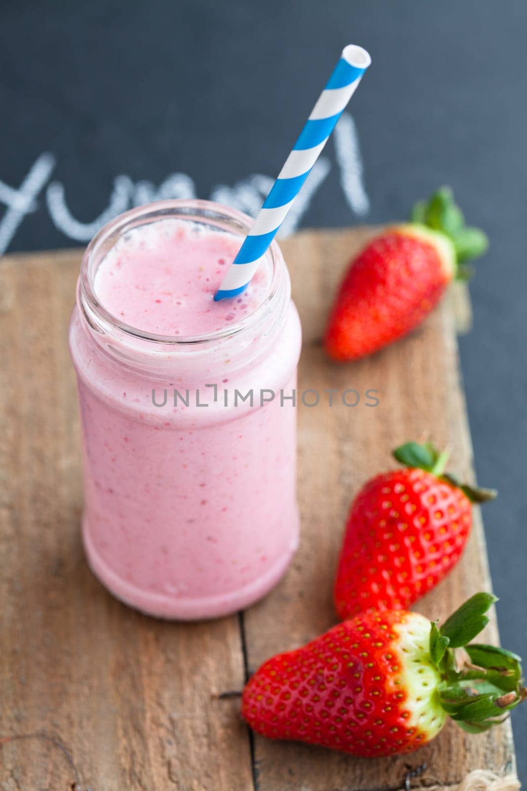 Strawberry smoothie with striped straw and whole strawberries on wooden serving tray