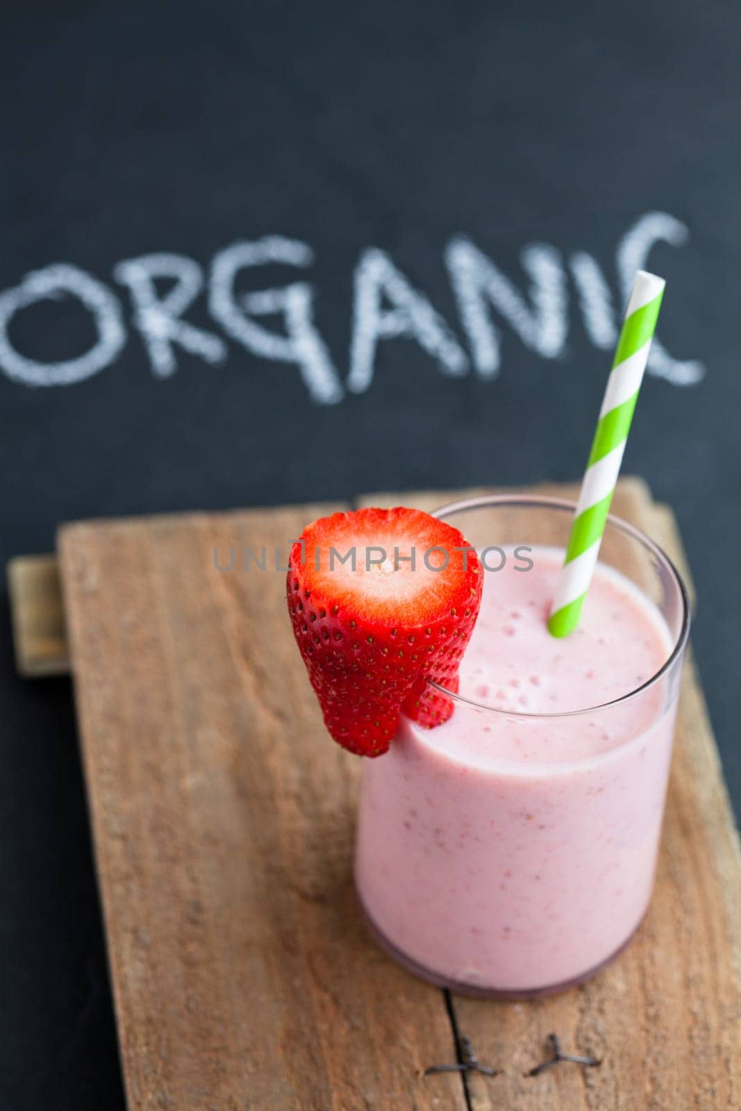Strawberry smoothie with striped straw and sliced strawberry