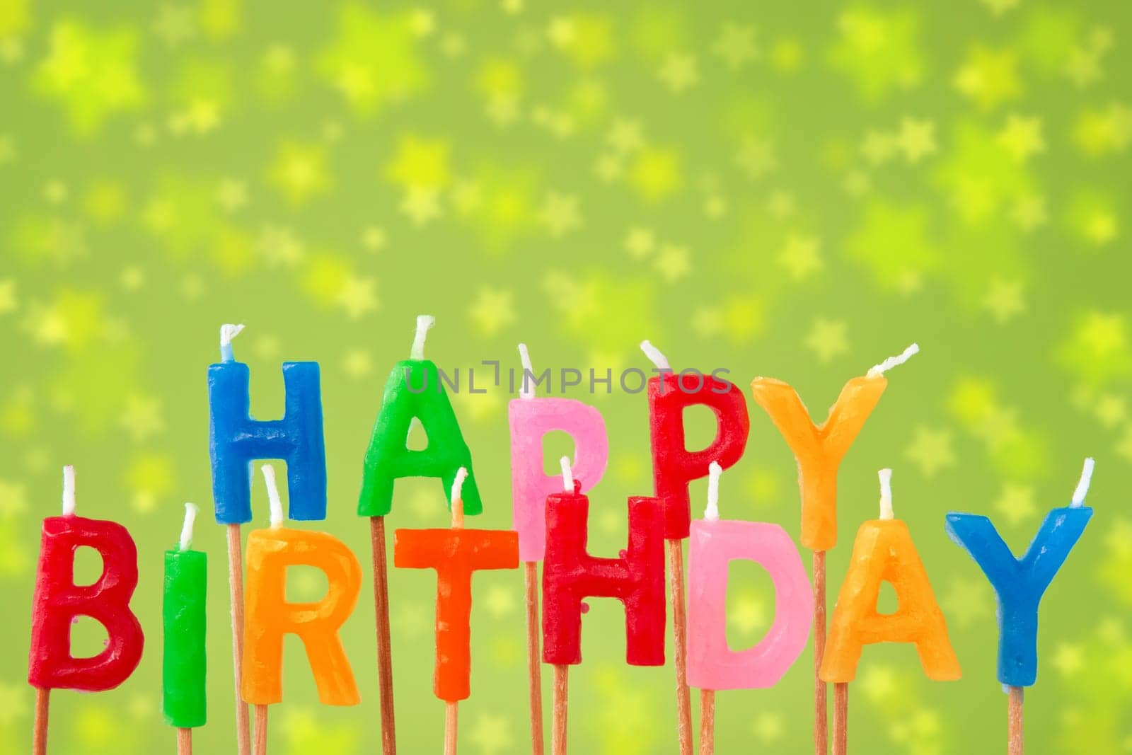Colorful candles forming the sentence "happy birthday"" on the green blurry background"