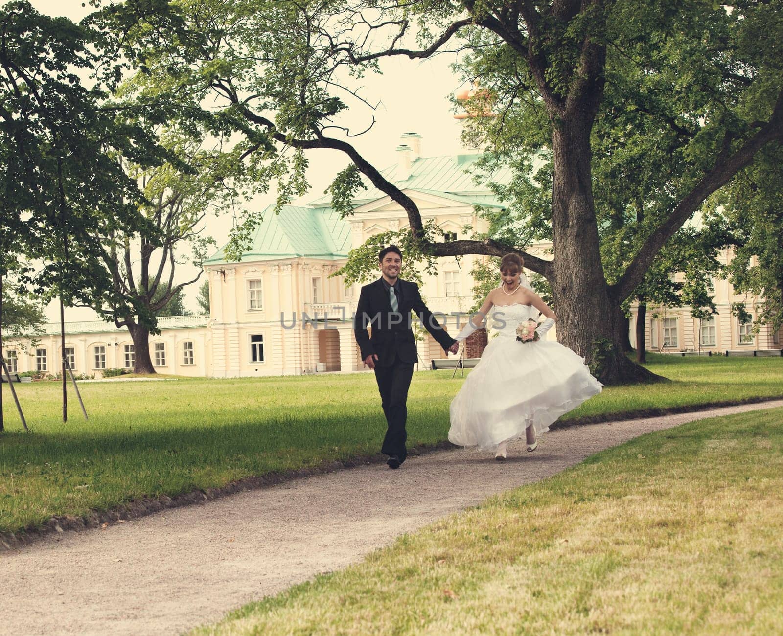 Groom and the bride run on a path in palace park
