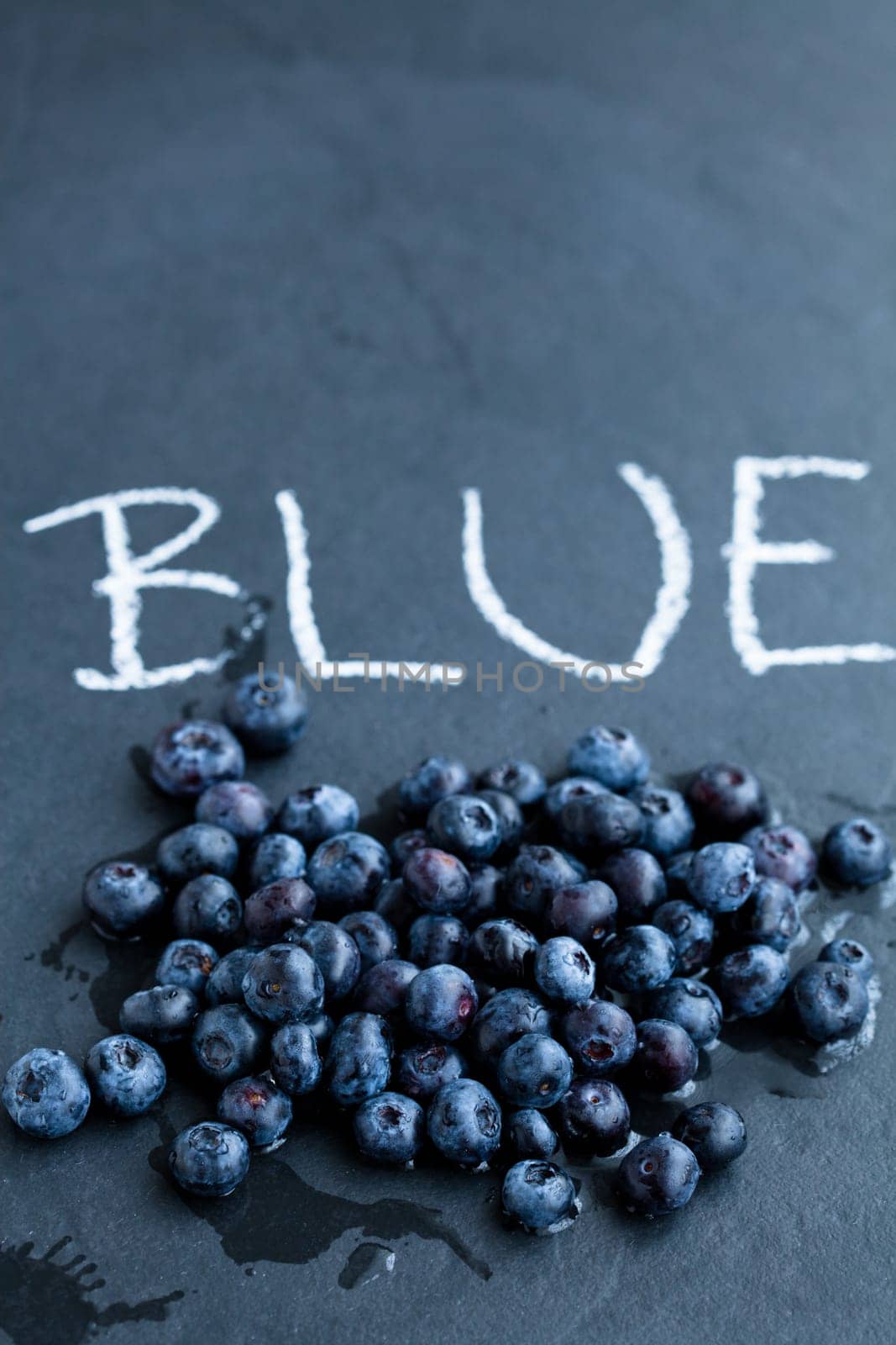 Fresh blueberries and word blue written in chalk on dark background