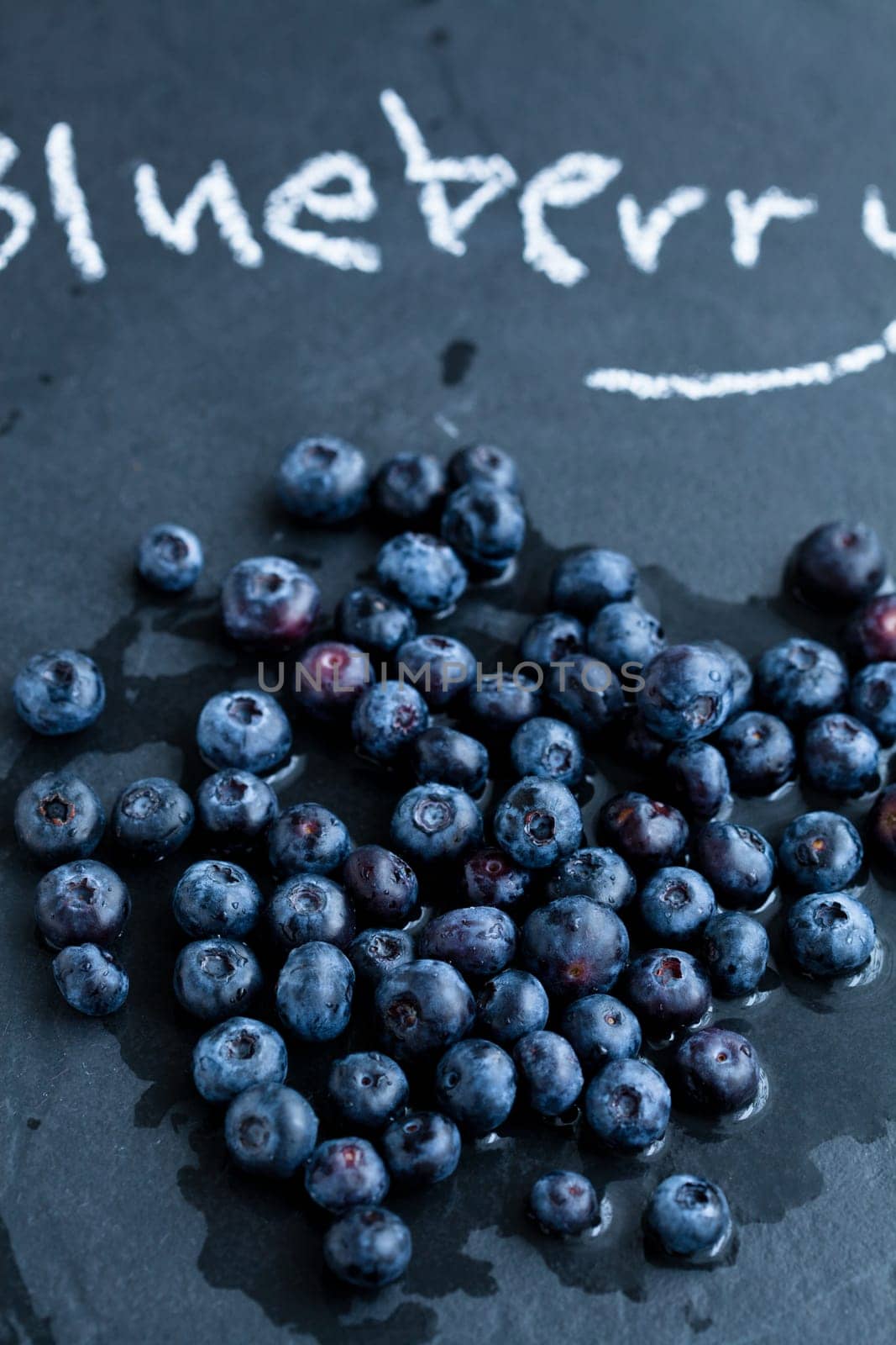 Closeup of fresh blueberries and word blueberry written in chalk on dark background