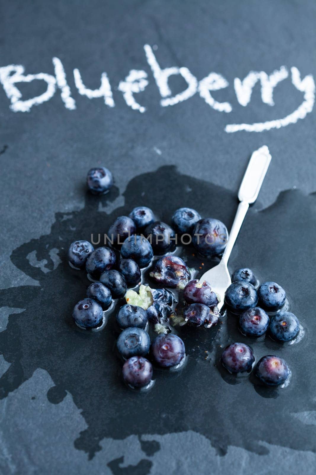 Fresh blueberries and fork and word blueberry written in chalk on dark background