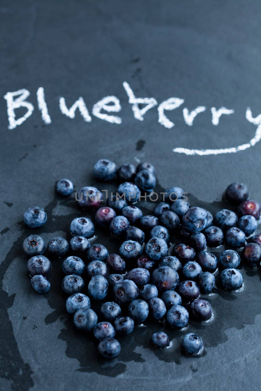 Fresh blueberries and word blueberry written in chalk on dark background