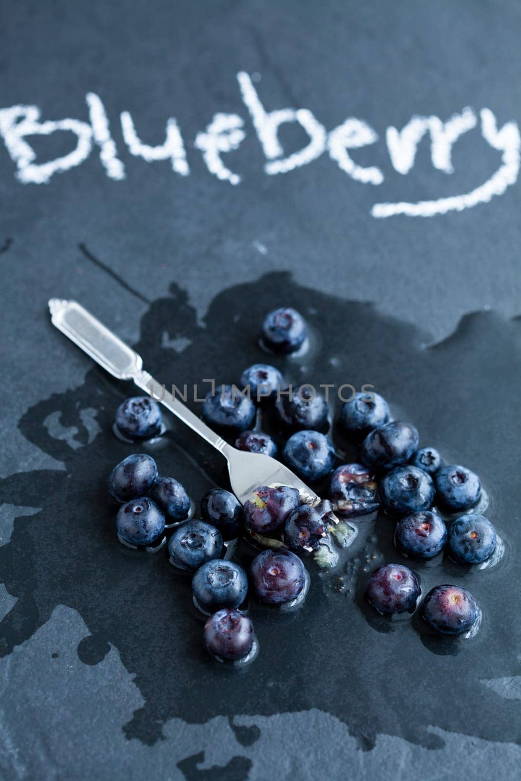 Fresh blueberries and fork and word blueberry written in chalk on dark background