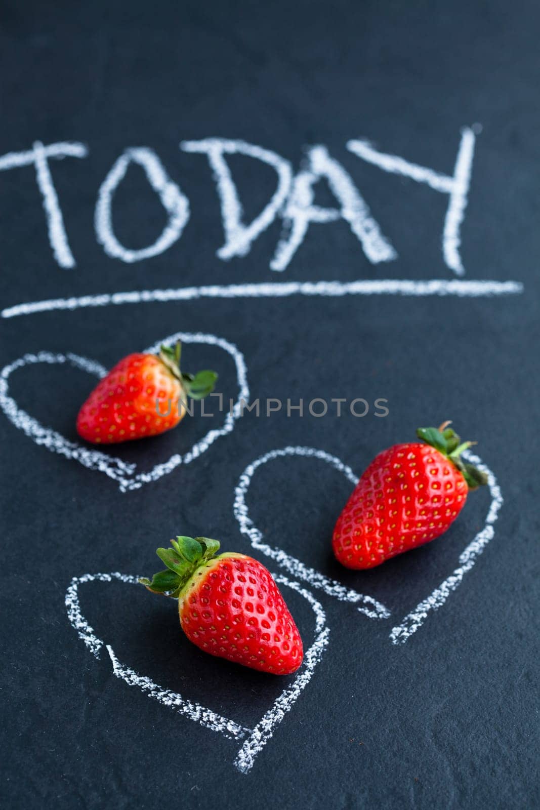 Three fresh whole strawberries inside chalk heart drawings and today word on dark background