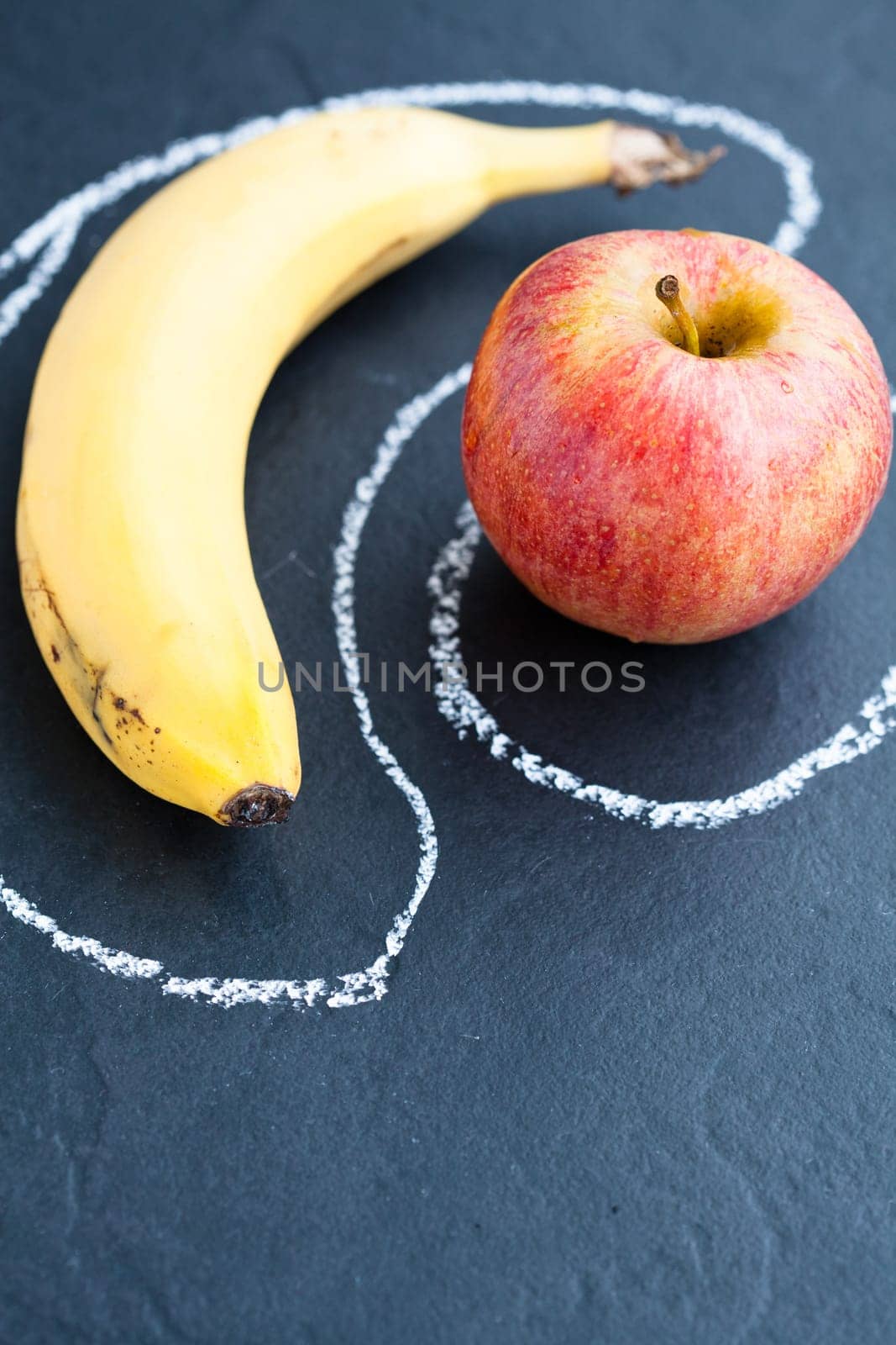 Closeup of apple and banana inside chalk outlines on dark background