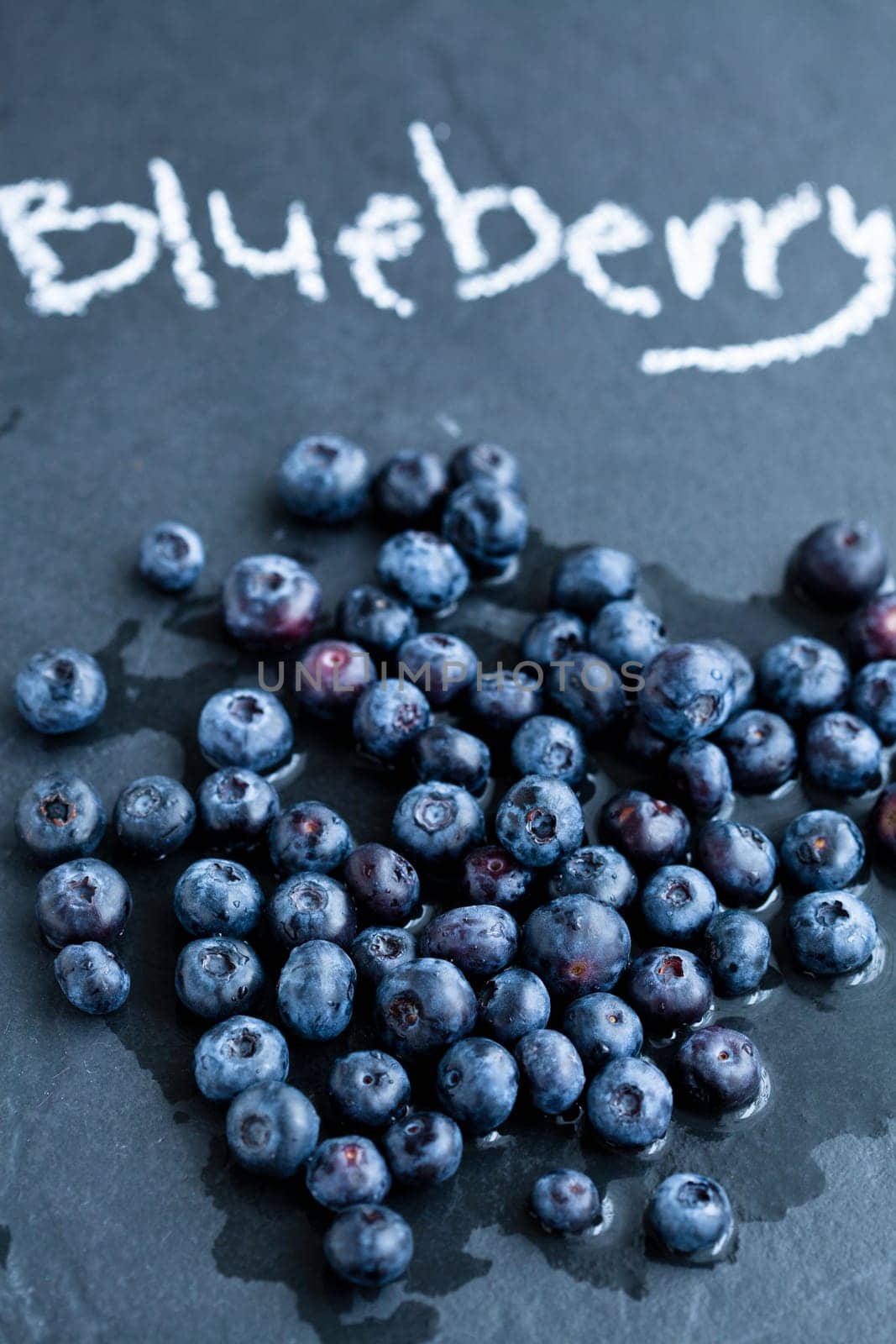 Closeup of fresh blueberries and word blueberry written in chalk on dark background