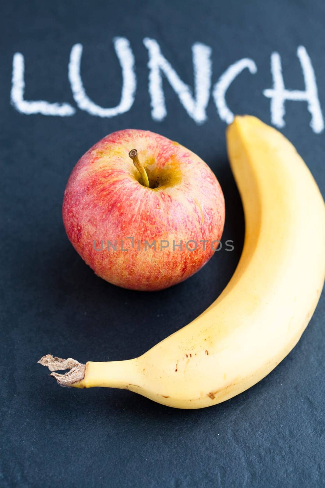 Closeup of apple and banana and word lunch written in chalk on dark background
