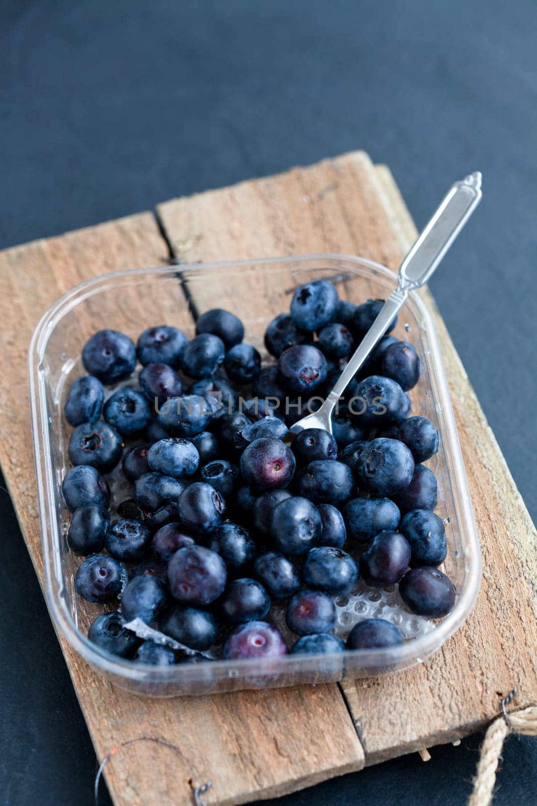 Closeup of fresh blueberries and fork on wooden serving tray on dark background