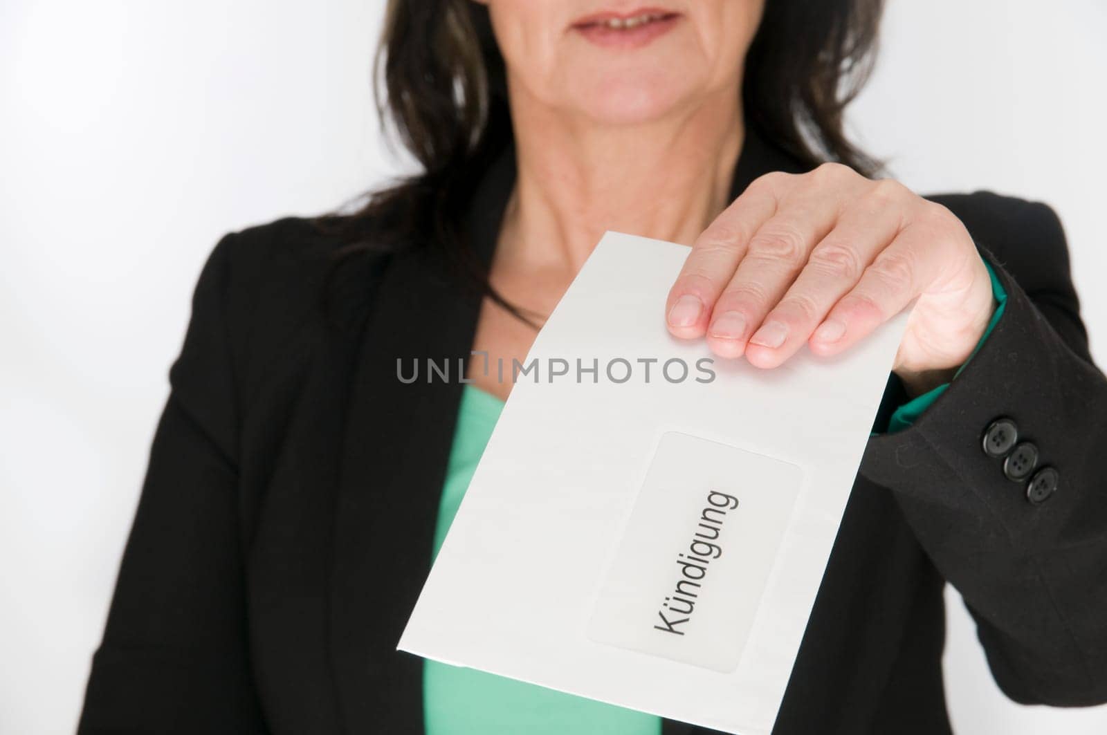 Upper-body shot of a middle-aged woman in front of a white studio background shows an envelope with the inscription "Resignation"" to the camera  Face from mouth upwards not in the picture"