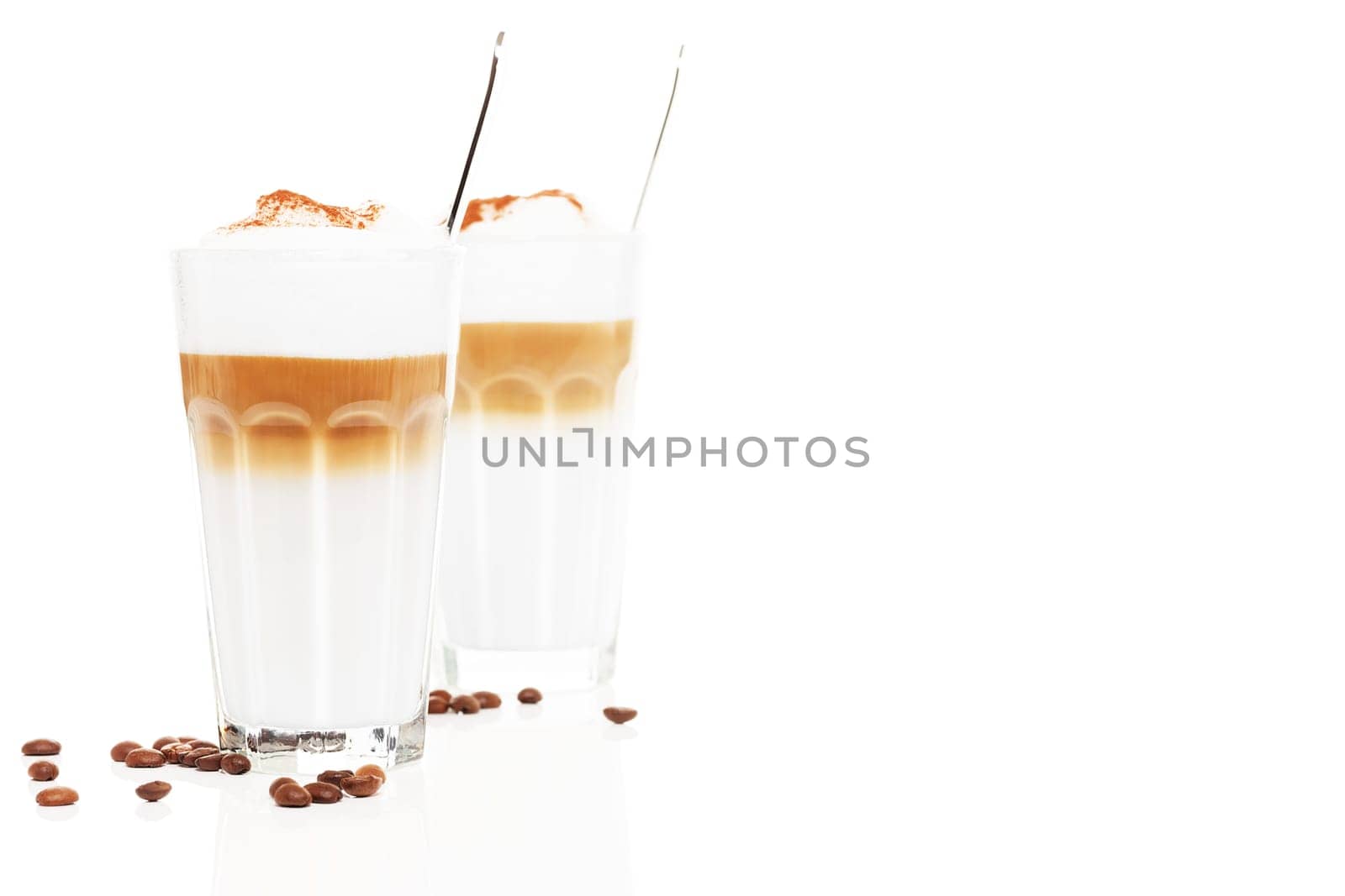 Latte macchiato in front of another latte Macchiato with coffee,beans and chocolate powder on white background