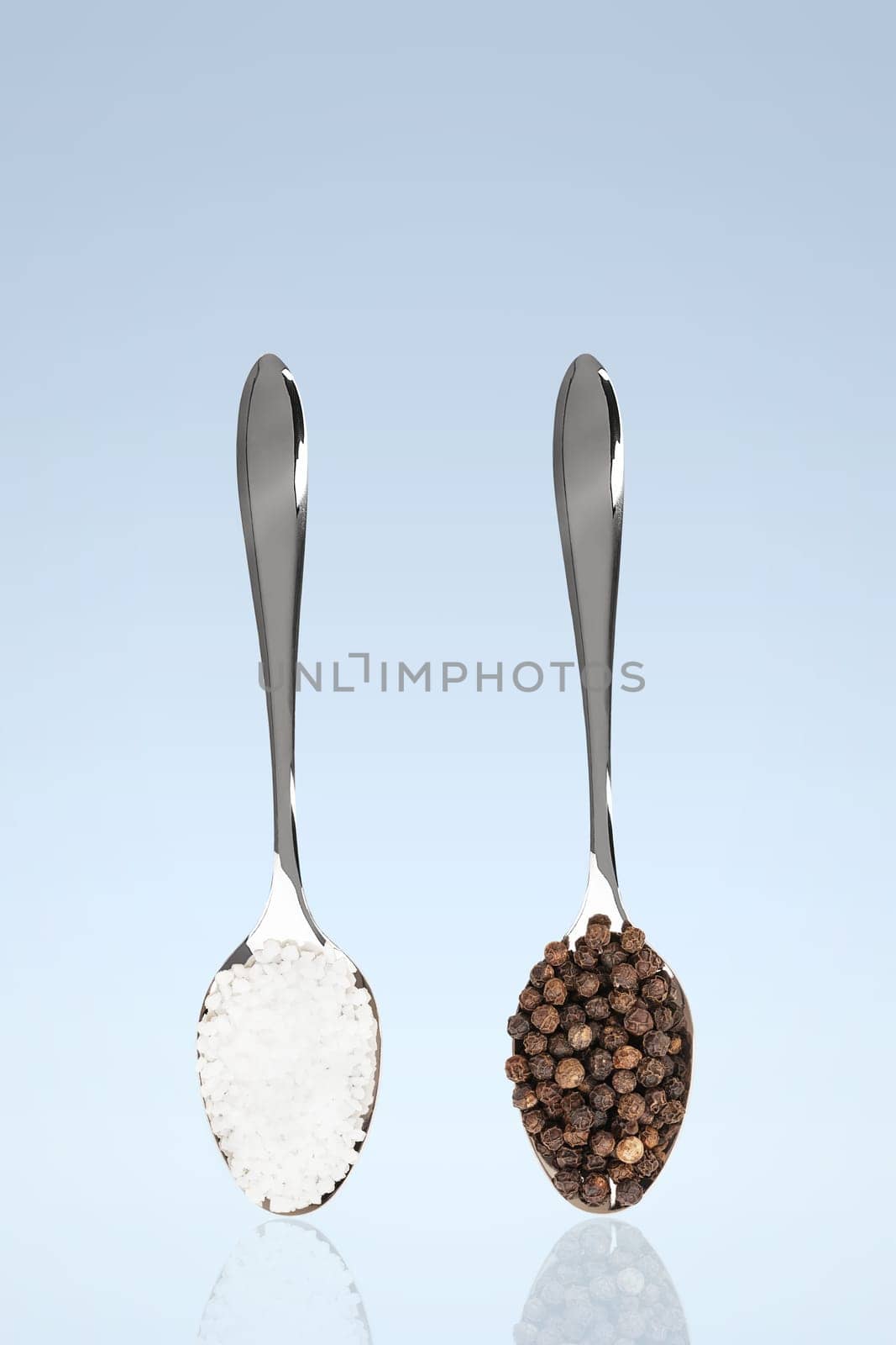 Salt and pepper on spoons against blue background