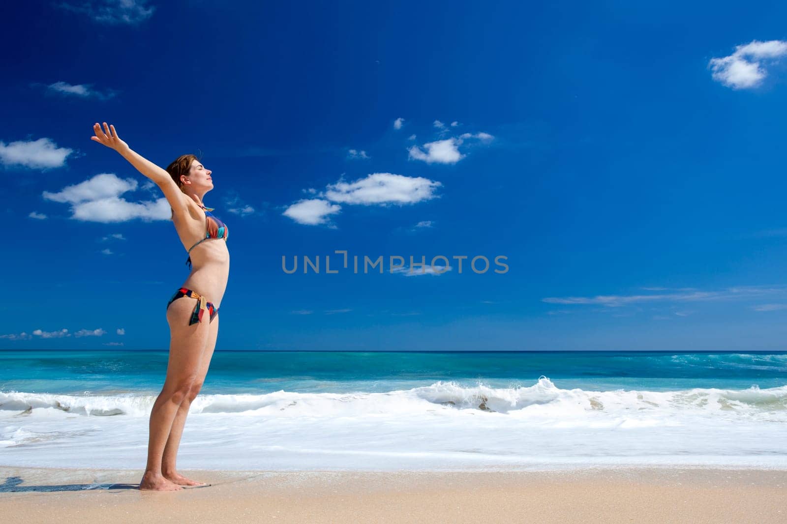 Beautiful young woman with arms open in a tropical beach enjoying the summer