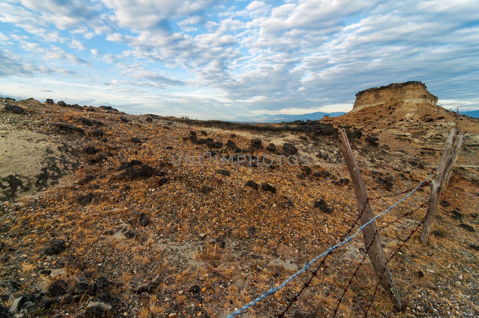 Fence extending in a rocky barren desert under a dramatic sky