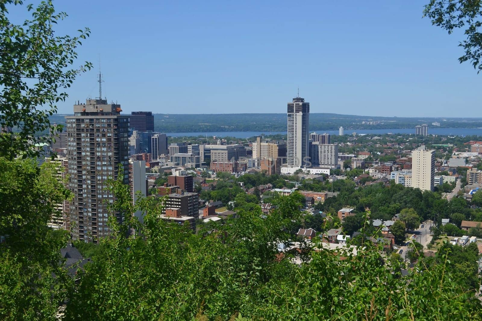 The view of downtown Hamilton with some high rises and a park in the foreground, and the lake Ontario in the background, from the mountain.