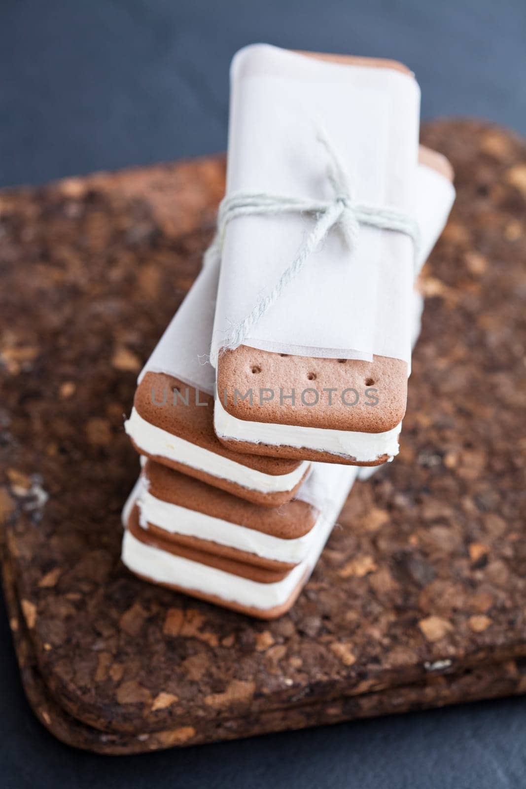 Closeup of stack of vanilla ice cream biscuits wrapped in white paper with string and bow resting on brown place mat