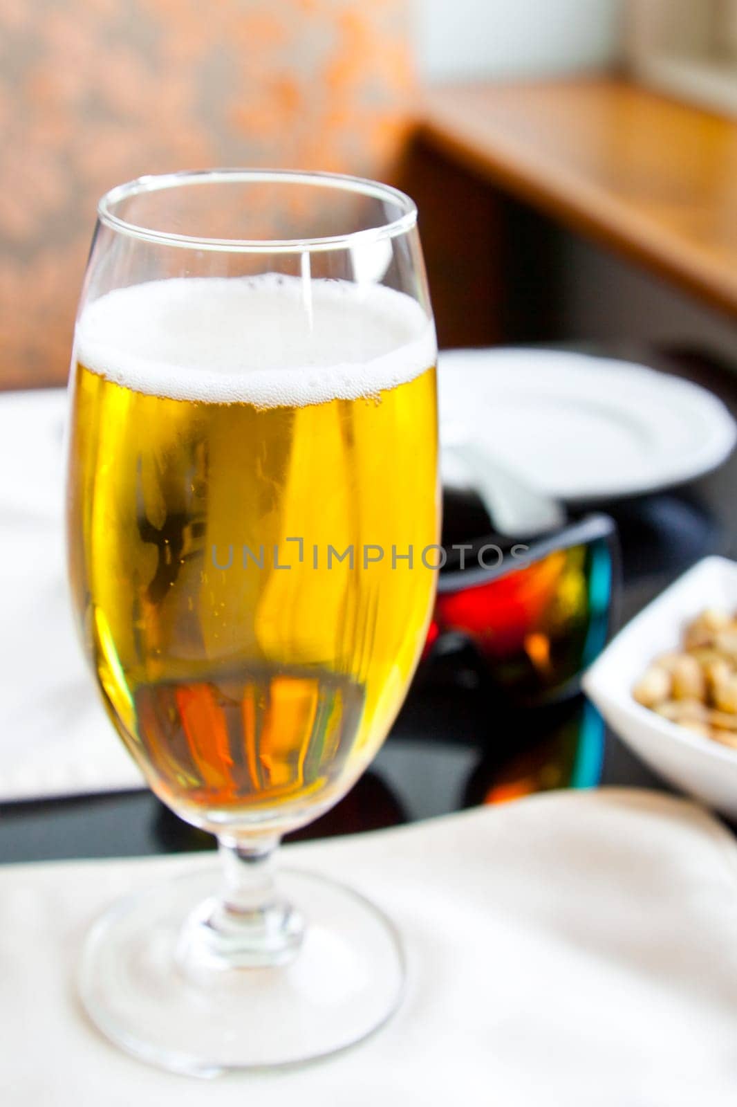 Vertical Interior corner detail of black top table with glass of beer, mirrored sunglasses by a window ledge in daylights with snacks close by