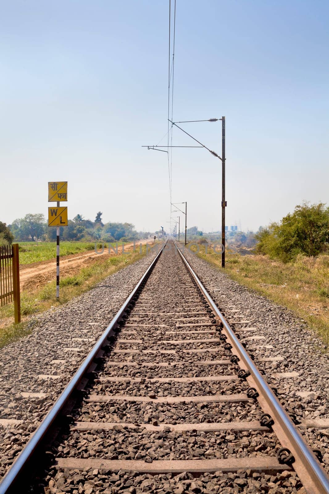 Vertical landscape of railroad tracks in Indian cutting acrosss the rural countryside along the outskirts of o Gujarat village towards the city of Surat. Typical scene with litter thrown around and locals walking close by
