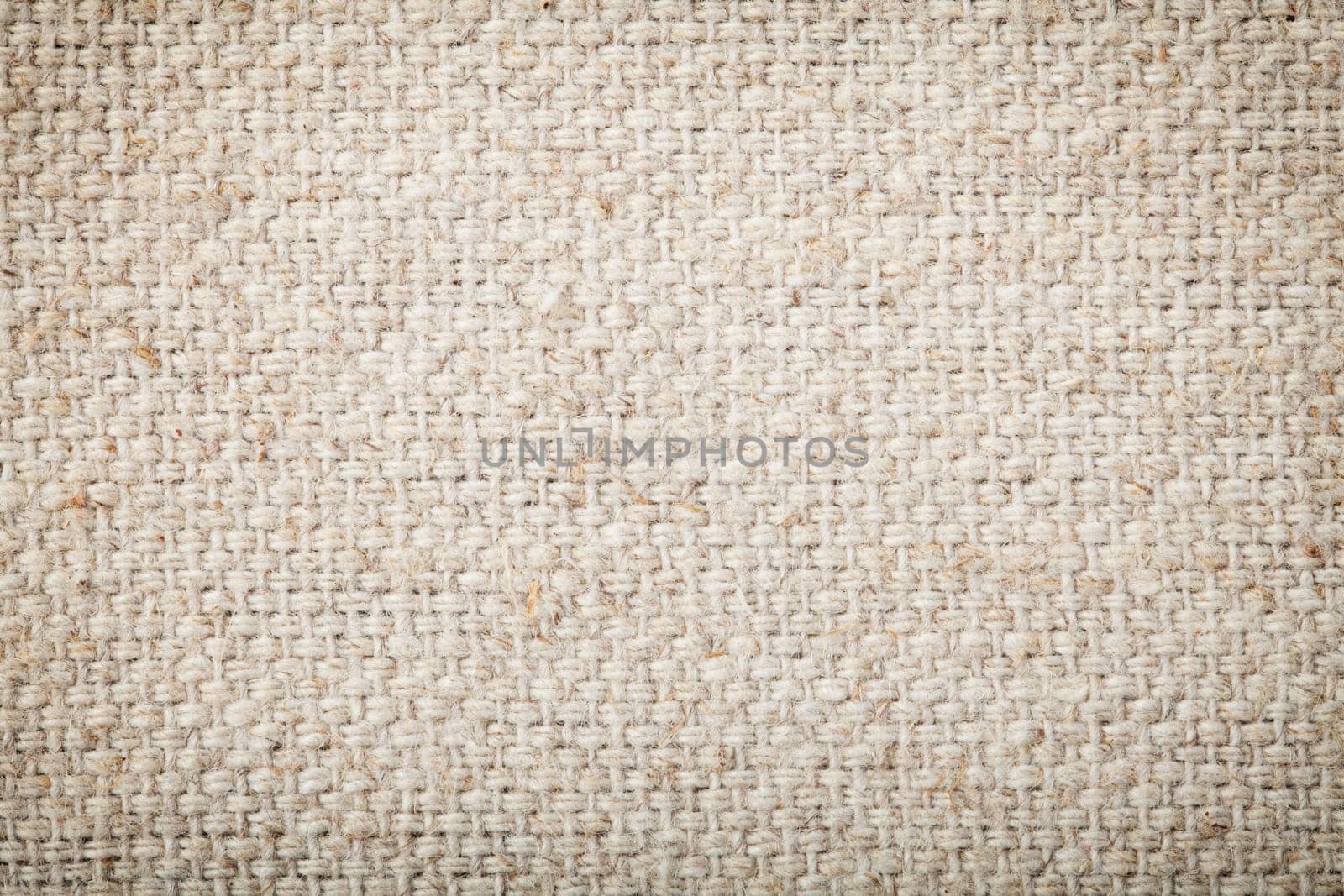 Background texture of natural unbleached woven canvas or burlap showing fibre and weave texture and pattern with light corner vignetting