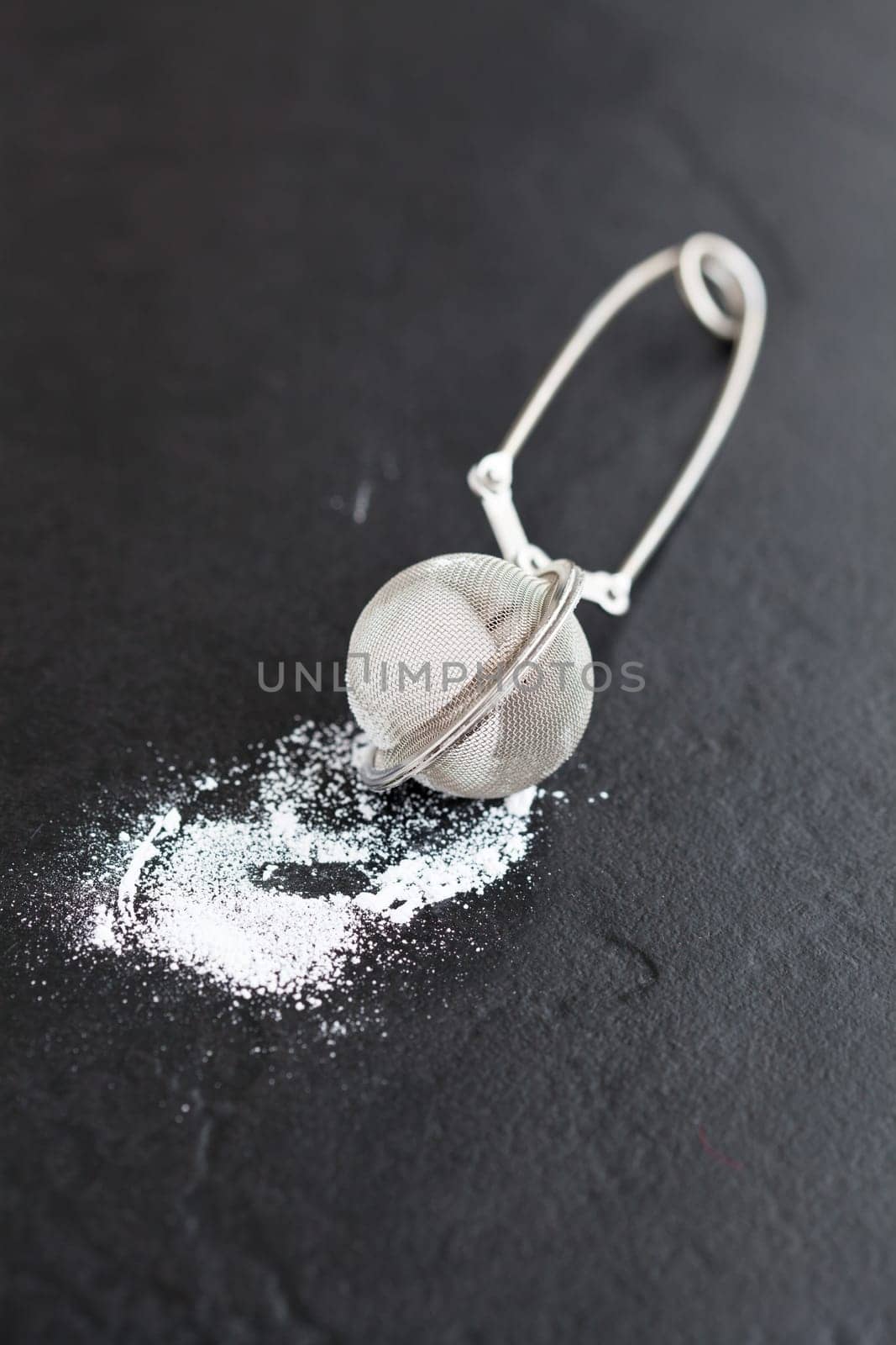 Closeup of sieve and icing sugar on dark textured background