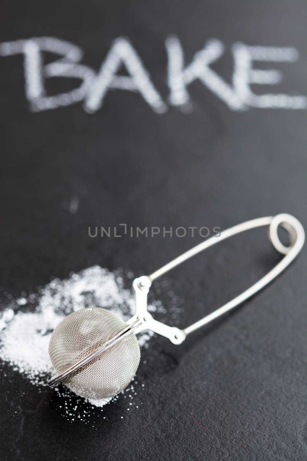 Closeup of sieve and icing sugar with word bake written in chalk on dark textured background