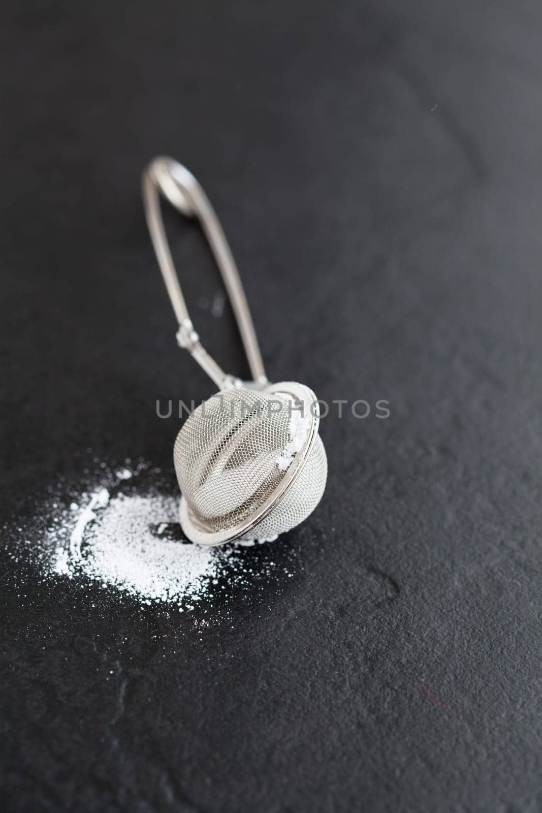 Closeup of sieve and icing sugar on dark textured background