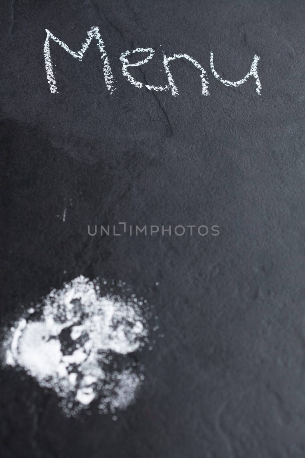 Closeup of dark background with icing sugar and word menu written in chalk