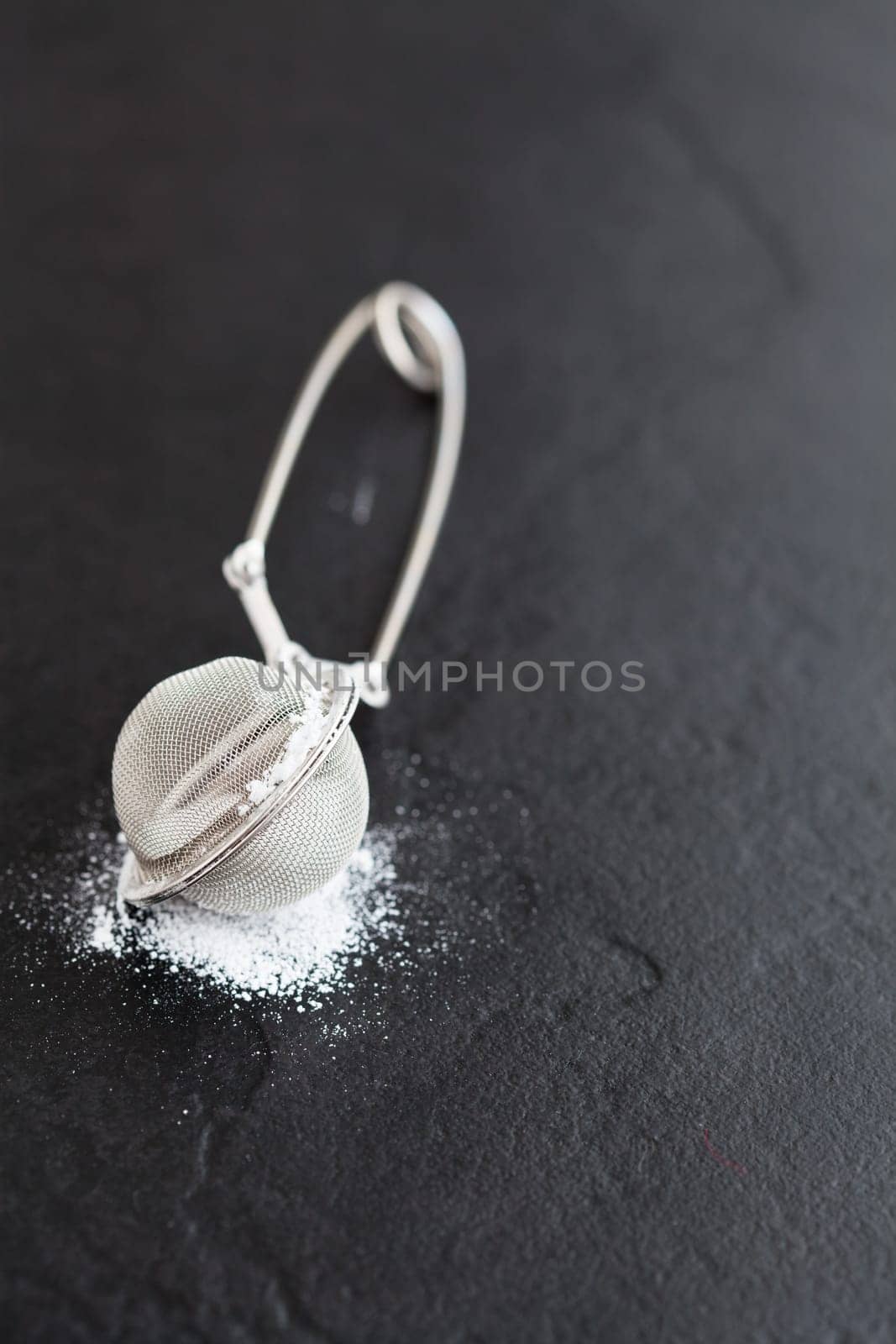 Closeup of sieve and icing sugar on dark textured background
