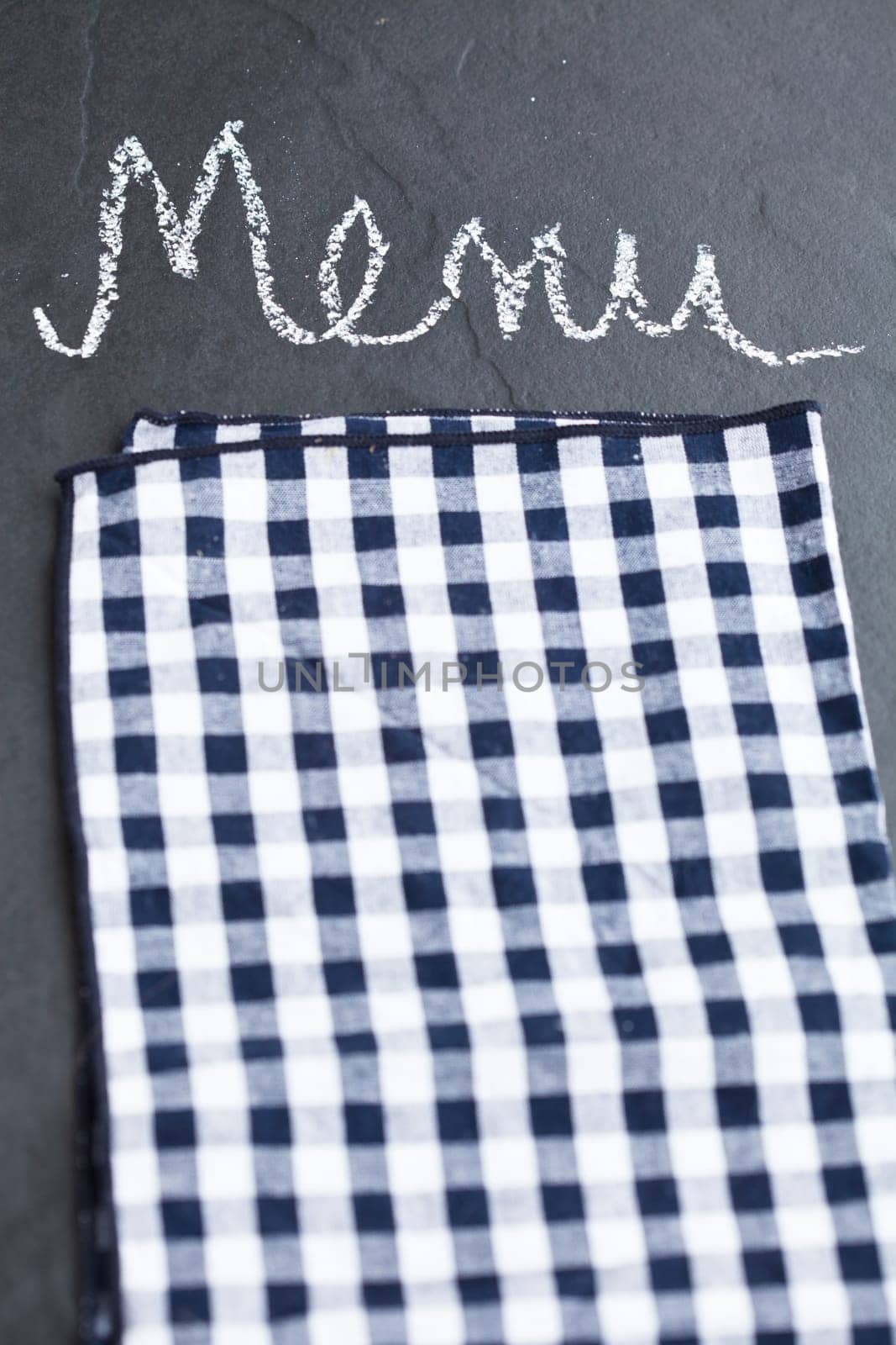 Closeup of checkered napkin and word menu written in chalk on dark background