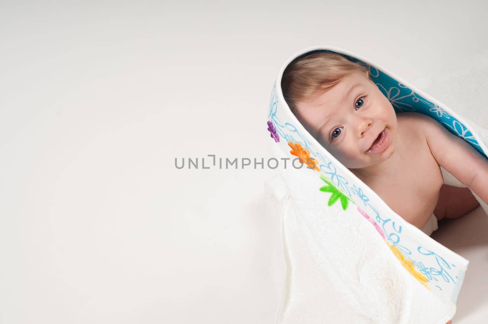 Happy little boy in white blanket with flowers in studio