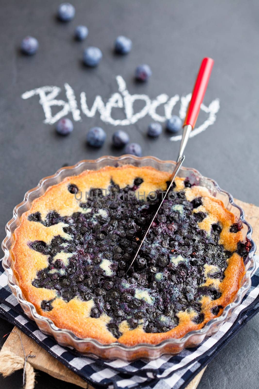 Blueberry pie in glass dish and server with word blueberry written in chalk on dark background