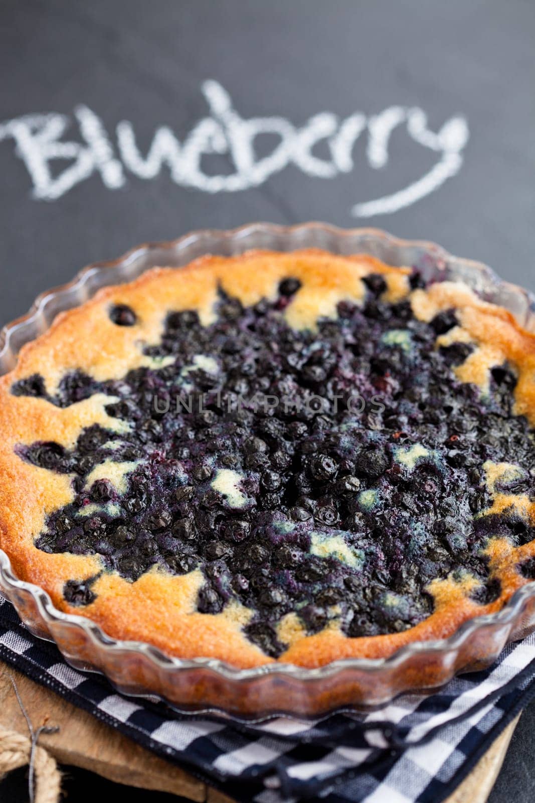 Closeup of blueberry pie in glass dish with word blueberry written in chalk on dark background