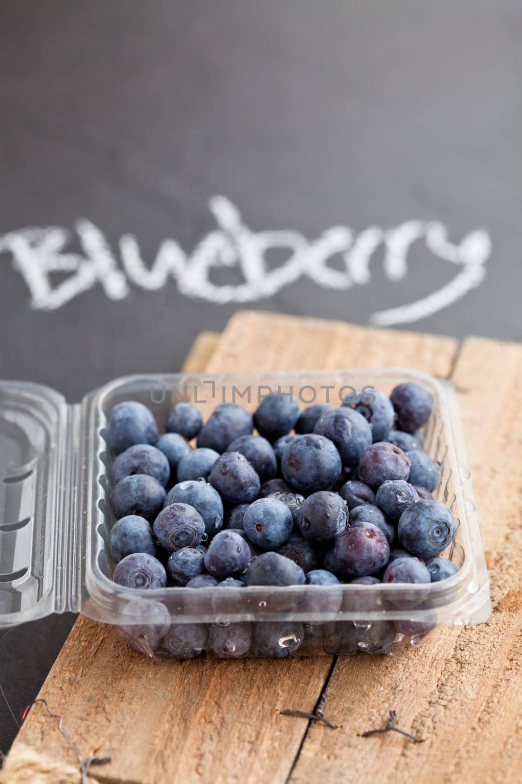 Fresh blueberries in plastic container on wooden serving surface with word blueberry written in chalk on dark surface