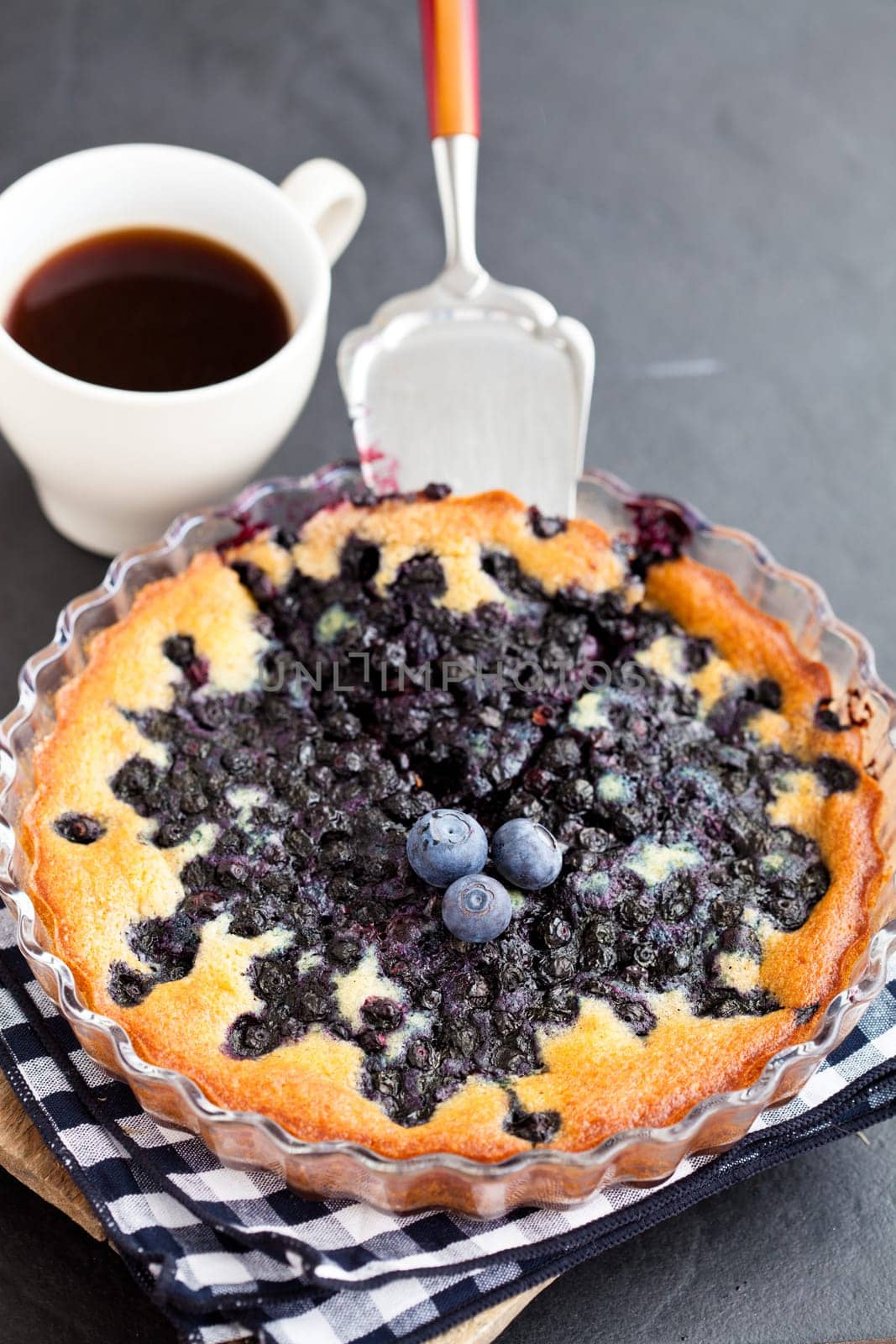 Blueberry pie in glass dish and server and coffee in white cup