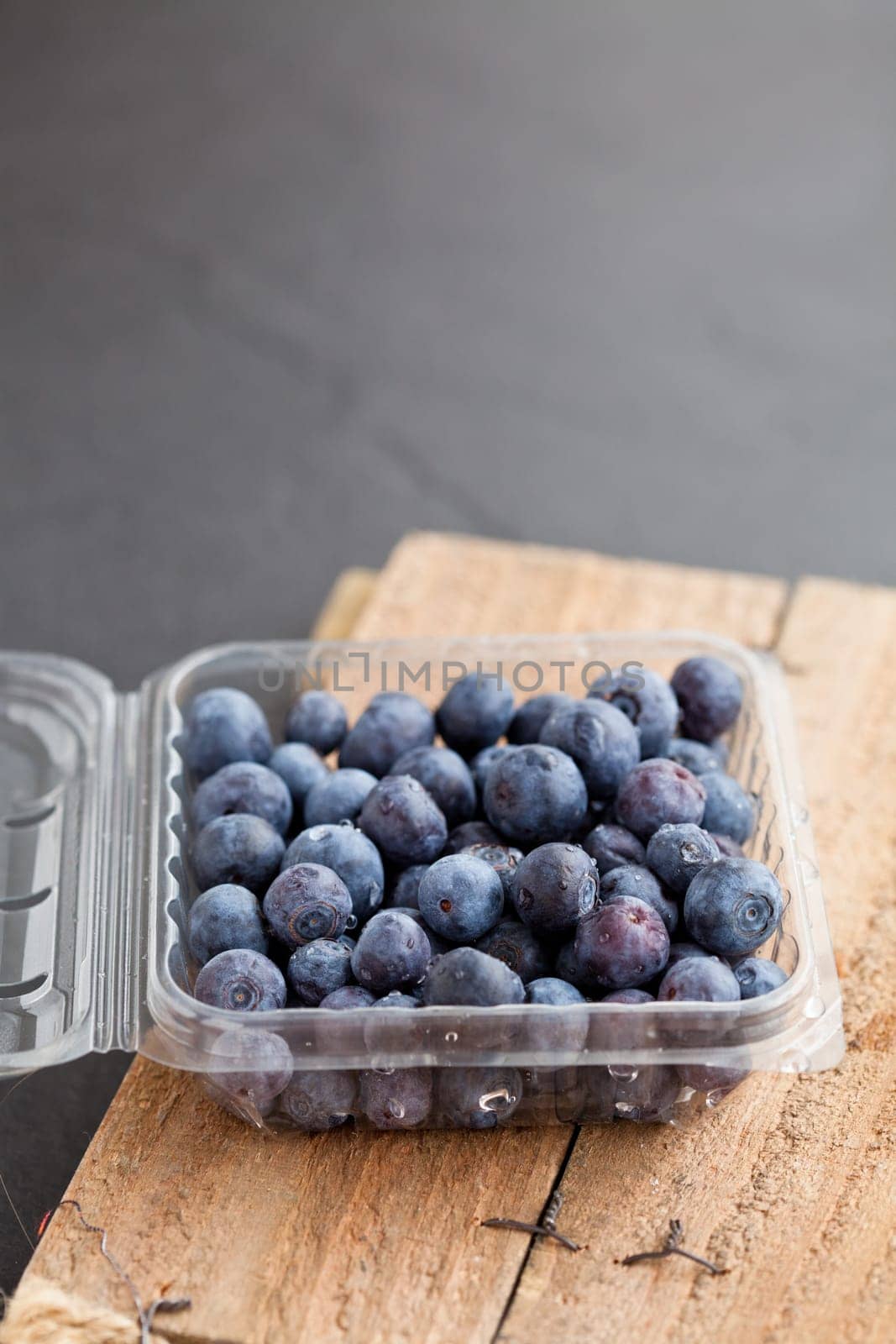 Closeup of fresh blueberries in plastic container resting on wooden serving surface