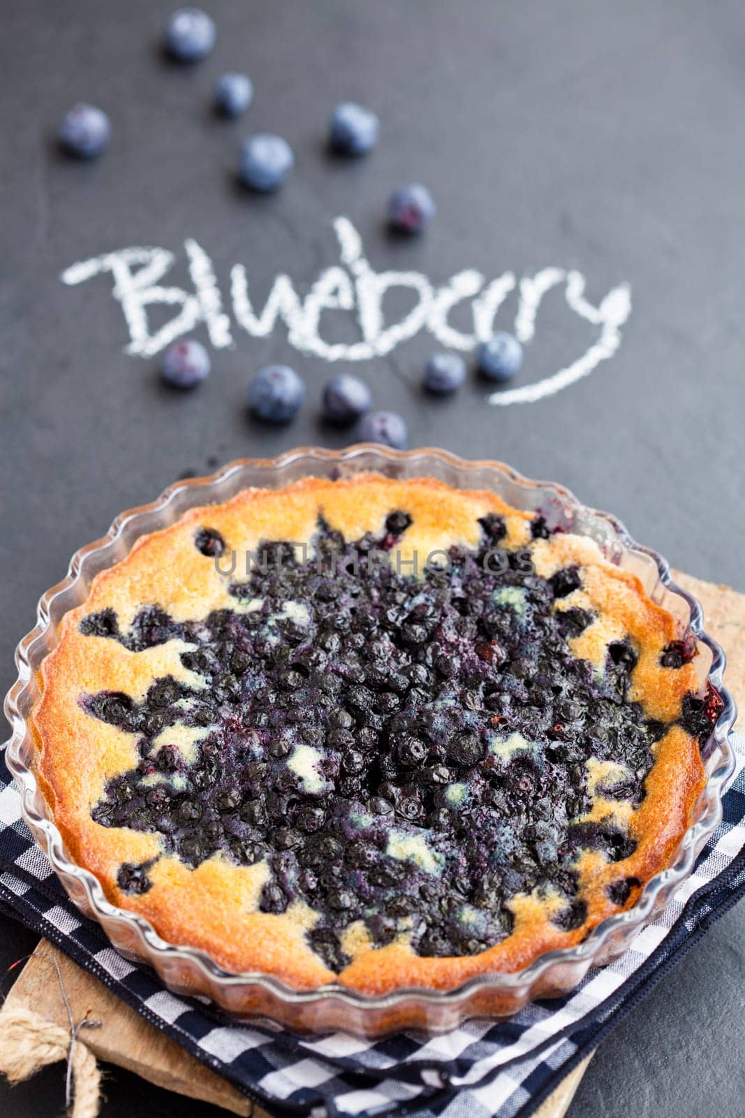 Blueberry pie in glass dish with word blueberry written in chalk on dark background