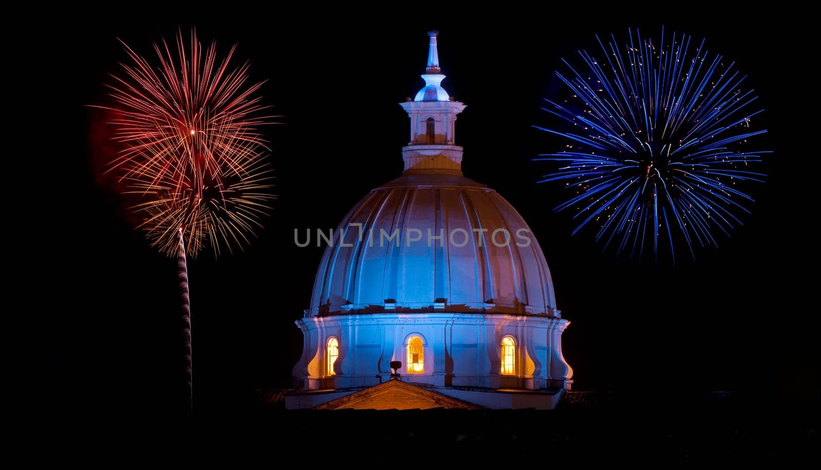 The dome of the cathedrel in Popayan, Colombia at night with blue and red fireworks going off