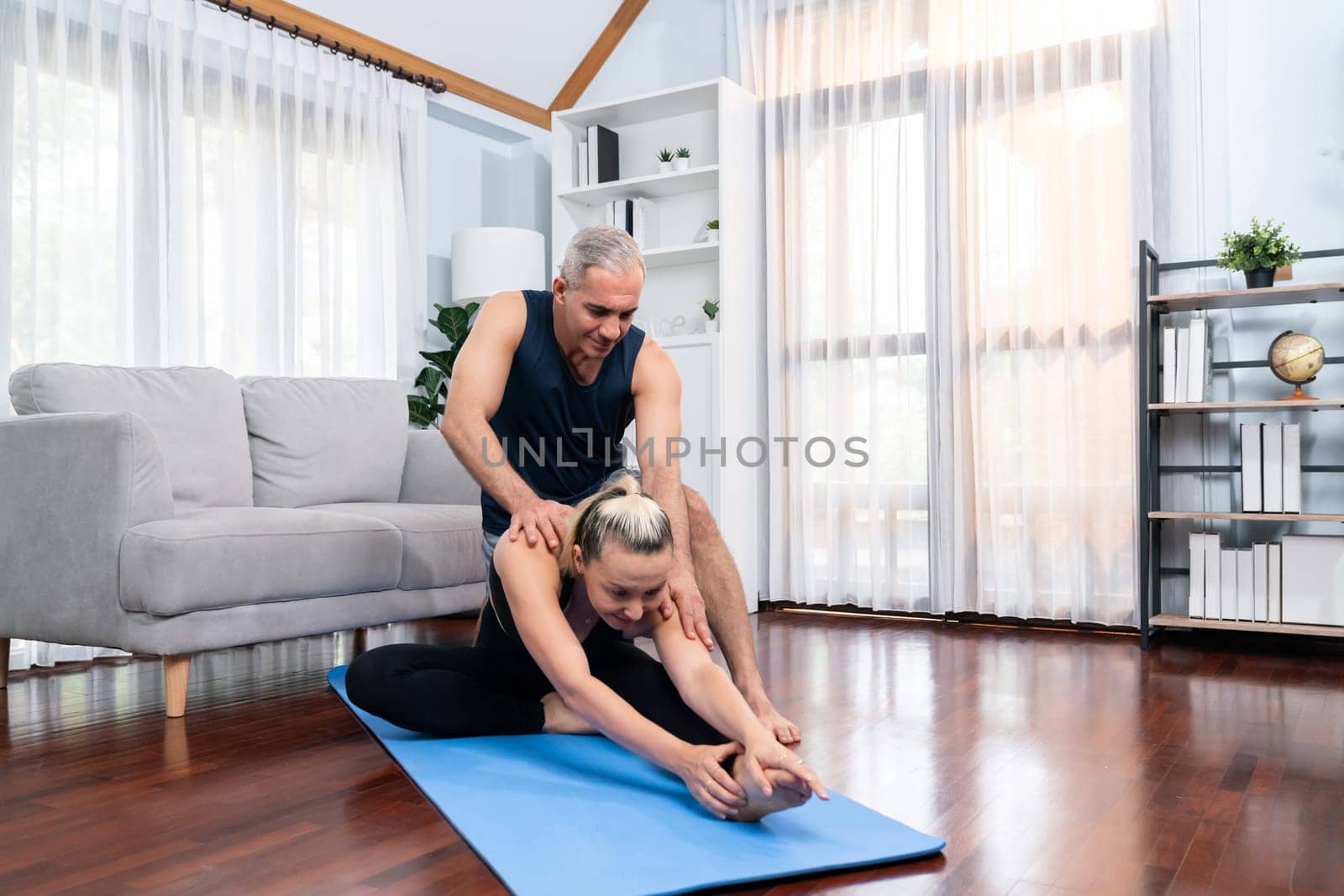 Happy active senior couple in sportswear being supportive and assist on yoga posture together at home. Healthy senior man and woman lifestyle with yoga exercise. Clout