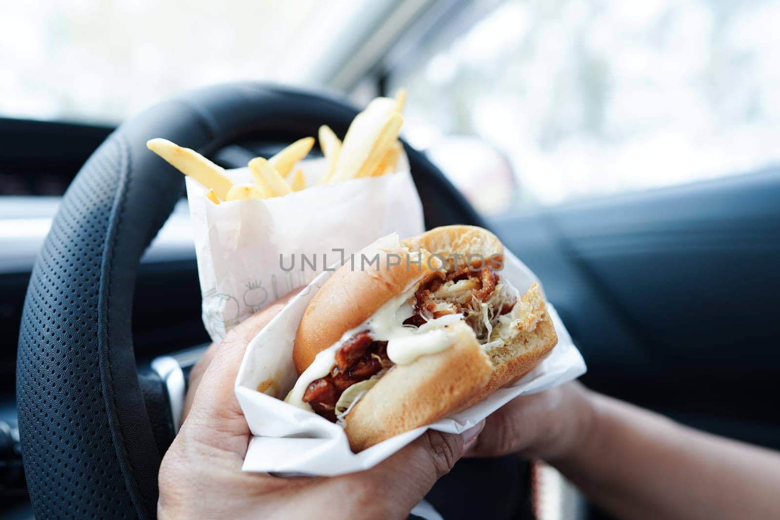 Asian woman driver hold and eat hamburger in car, dangerous and risk an accident. by sweettomato