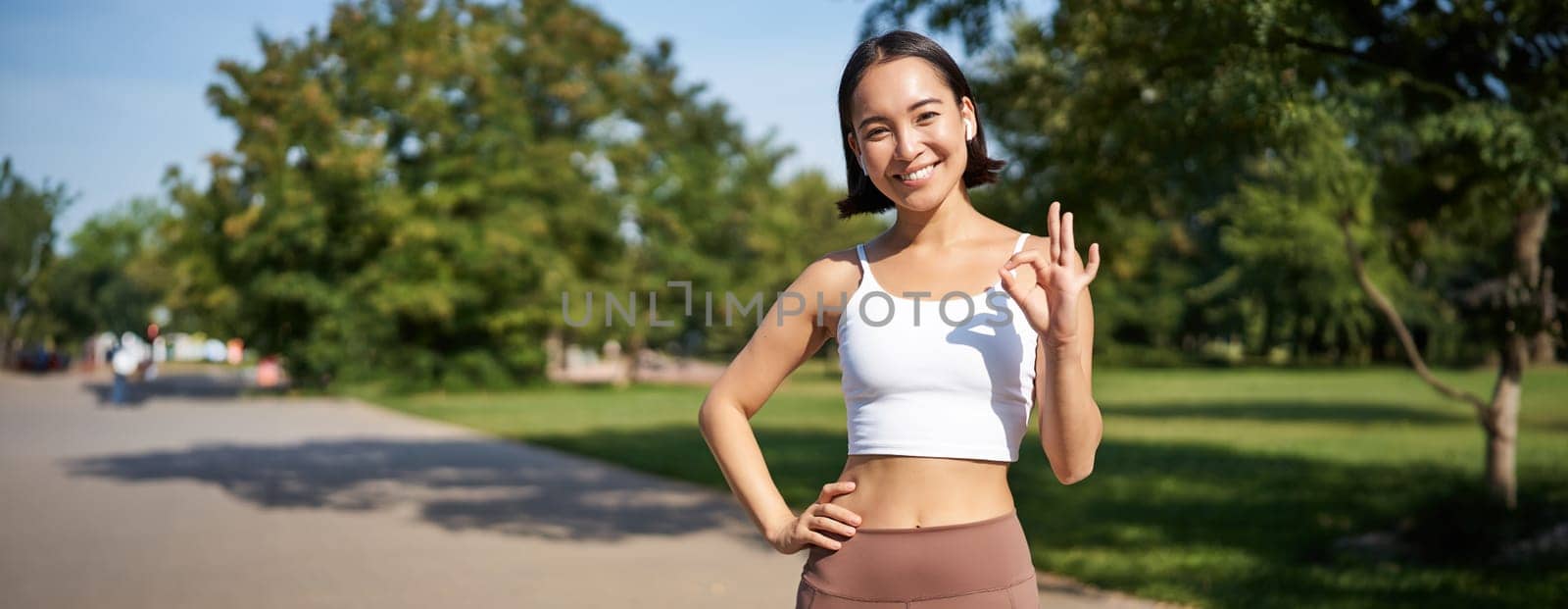Sport people. Happy asian girl, sportswoman showing okay sign and smiling, workout in gym, say yes, approve workout outdoors.