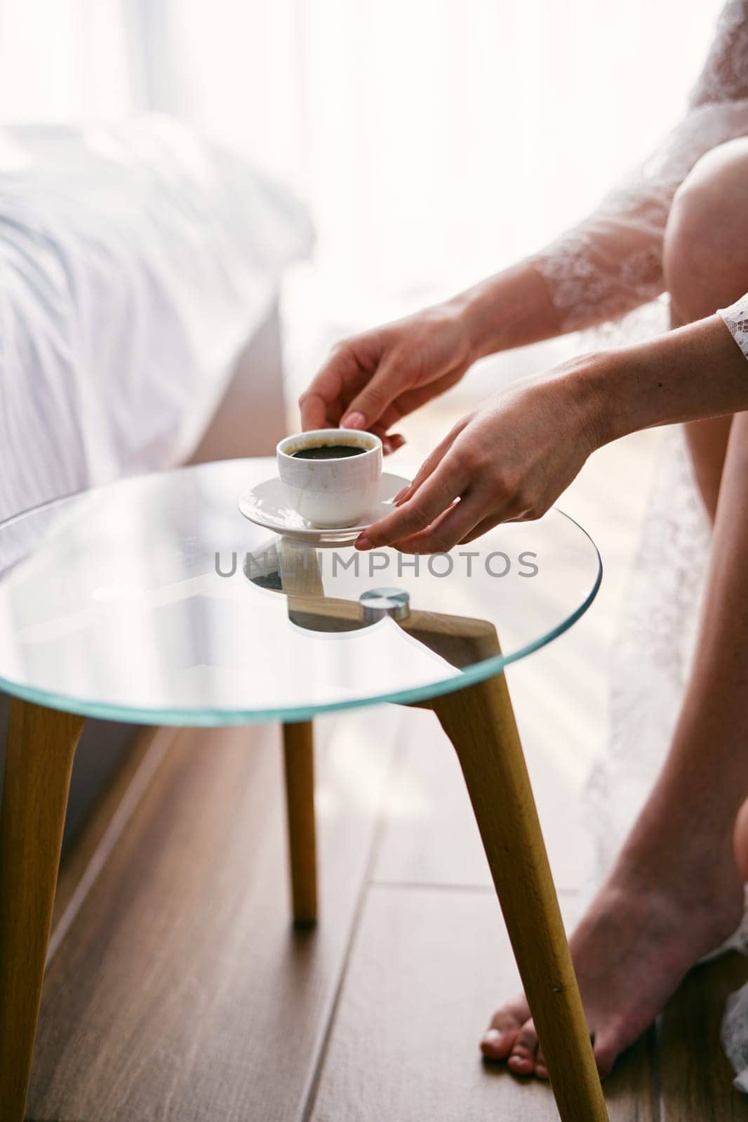 Bride takes a cup of coffee from a glass table while sitting in an armchair. Cropped. Faceless. High quality photo