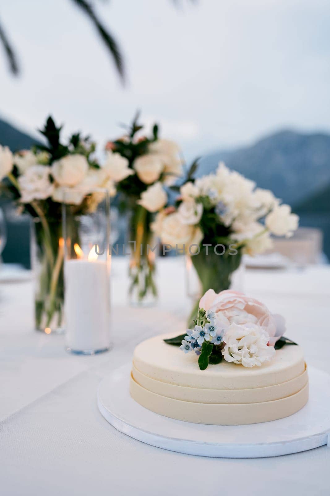 Wedding cake decorated with flowers stands on a plate on the table by Nadtochiy