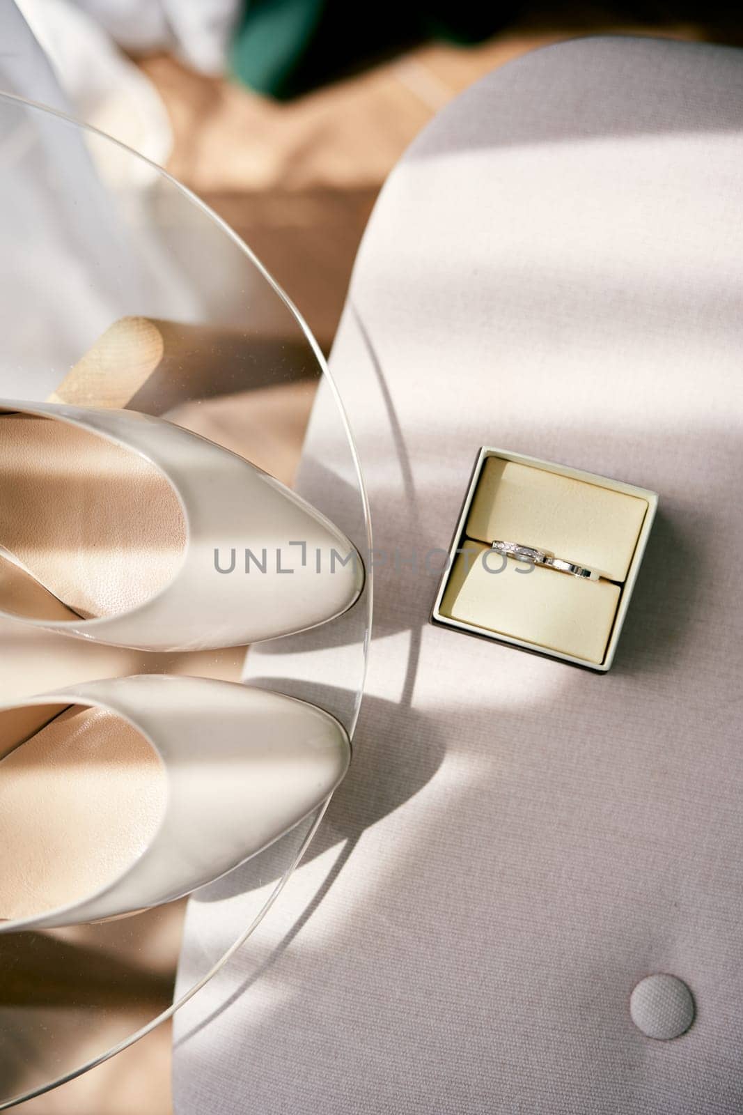 Box of wedding rings stands on a chair next to the table with the bride shoes by Nadtochiy