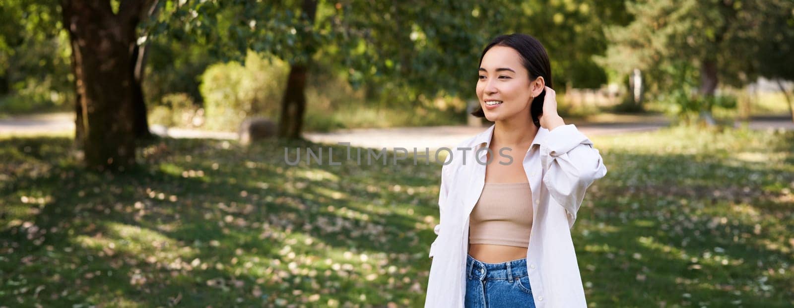 Beautiful young asian girl smiling, laughing and walking along park, enjoying summer sunny day. People and lifestyle concept