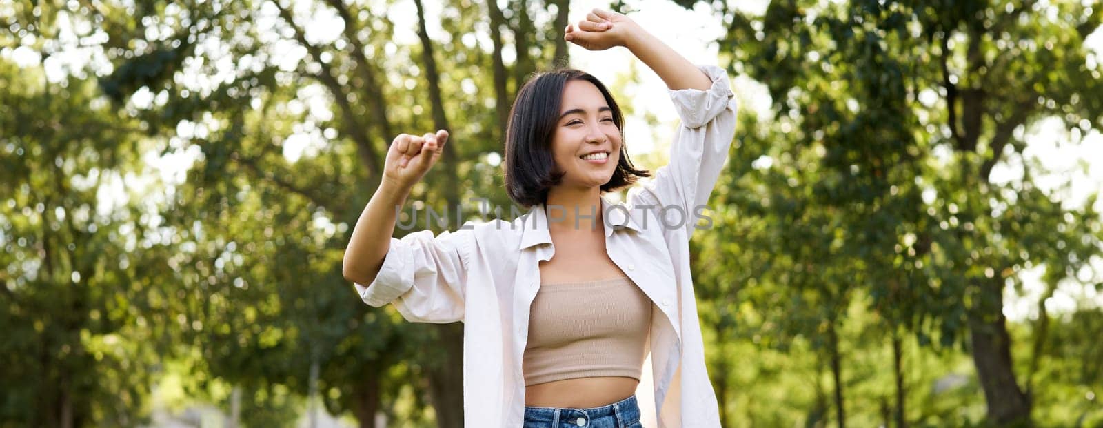 Carefree woman dancing and walking in park with hands lifted up high, smiling happily. Lifestyle concept.